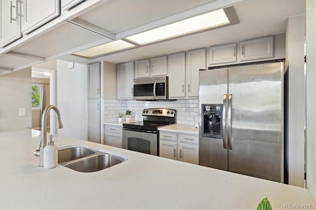 kitchen with appliances with stainless steel finishes, a sink, light countertops, and backsplash