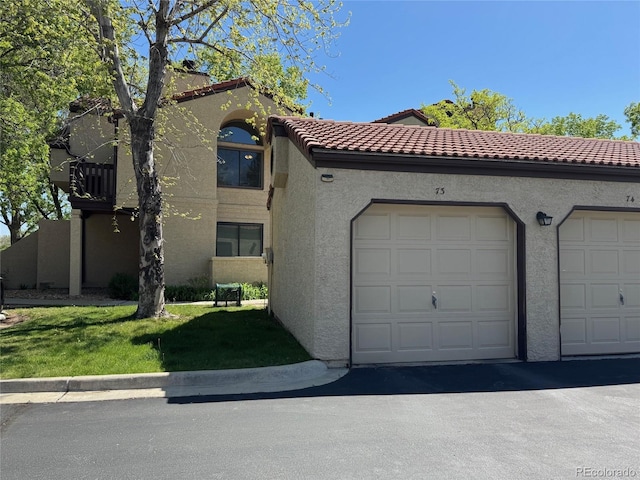 view of front of house with stucco siding, community garages, a tiled roof, and a front lawn