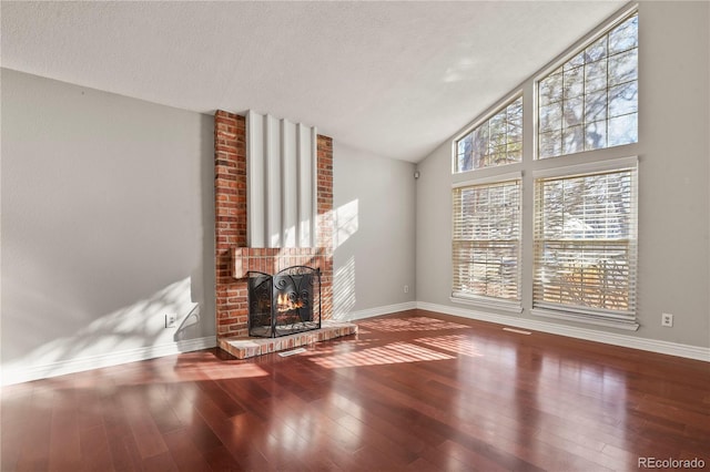 unfurnished living room with hardwood / wood-style flooring, high vaulted ceiling, a brick fireplace, and a textured ceiling