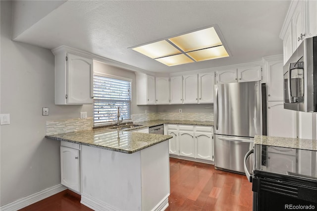 kitchen with sink, white cabinetry, stainless steel appliances, stone countertops, and kitchen peninsula