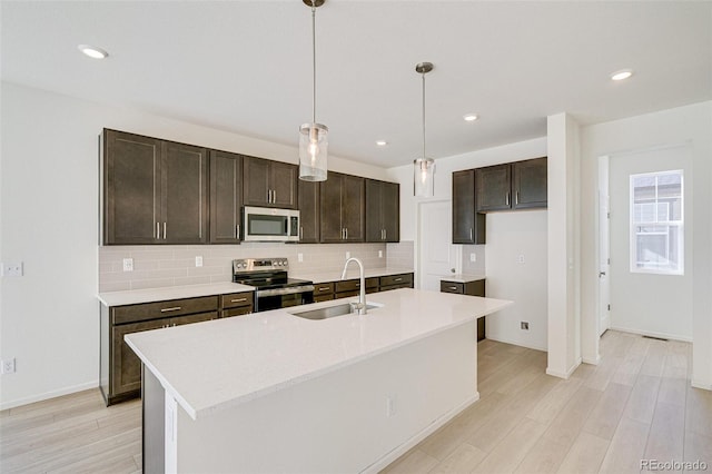 kitchen featuring sink, hanging light fixtures, an island with sink, light hardwood / wood-style floors, and stainless steel appliances