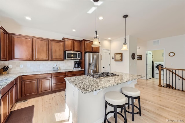 kitchen with washer / clothes dryer, appliances with stainless steel finishes, light wood-type flooring, and a kitchen island