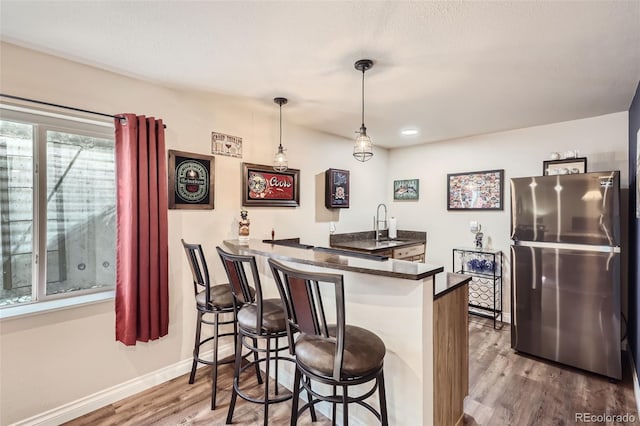 bar with hanging light fixtures, stainless steel refrigerator, and hardwood / wood-style floors