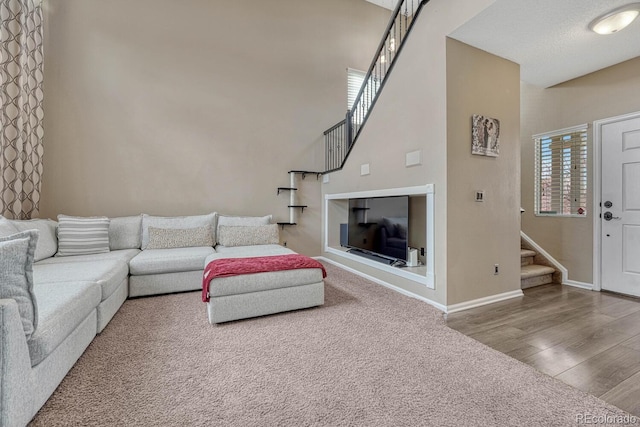 living room featuring a towering ceiling, baseboards, stairway, and wood finished floors