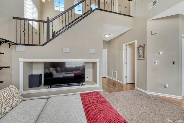 living room with a towering ceiling, wood finished floors, visible vents, and baseboards