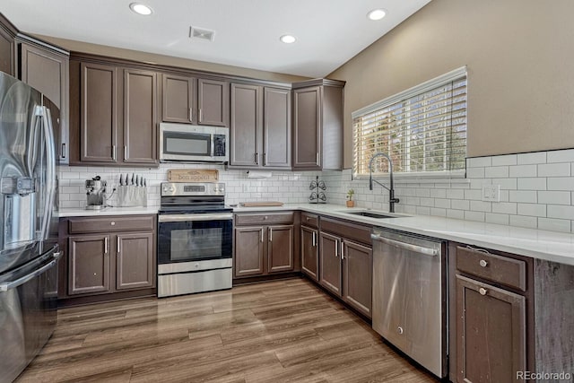 kitchen featuring stainless steel appliances, wood finished floors, a sink, visible vents, and backsplash