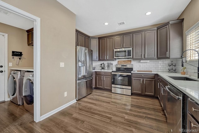 kitchen featuring visible vents, dark wood-style floors, washing machine and clothes dryer, stainless steel appliances, and a sink