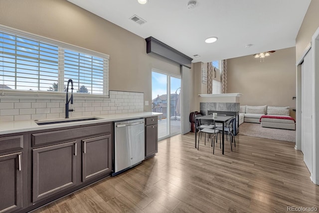 kitchen with tasteful backsplash, visible vents, light wood-type flooring, stainless steel dishwasher, and a sink