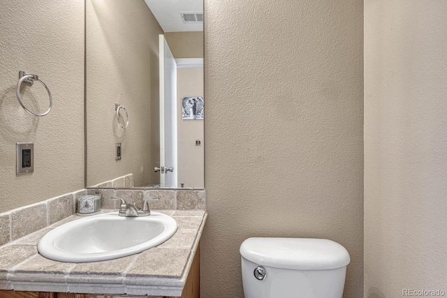 half bath with toilet, a textured wall, visible vents, and vanity