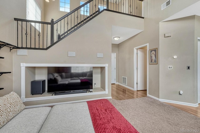living area with a high ceiling, wood finished floors, visible vents, and baseboards