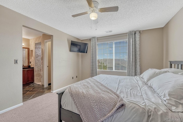 carpeted bedroom with a textured ceiling, ceiling fan, baseboards, ensuite bath, and visible vents