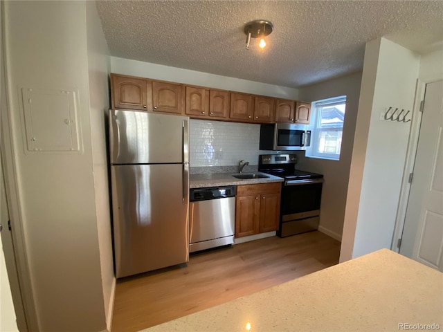 kitchen with sink, tasteful backsplash, a textured ceiling, light wood-type flooring, and stainless steel appliances