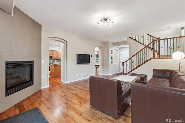 12427 James Ct, Broomfield, CO 80020 - living area featuring arched walkways, light wood-style floors, a glass covered fireplace, and stairway