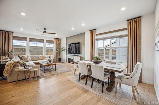 dining room with a glass covered fireplace, ceiling fan, light wood-style flooring, and recessed lighting