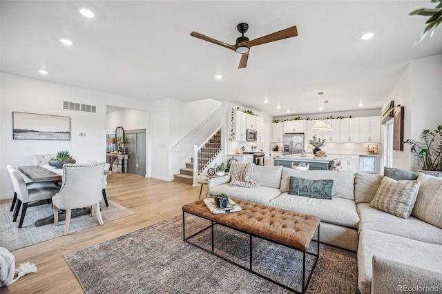 living room with light wood finished floors, baseboards, visible vents, stairs, and recessed lighting