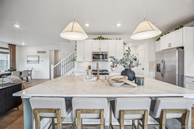 kitchen with stainless steel appliances, tasteful backsplash, visible vents, a kitchen island with sink, and white cabinetry