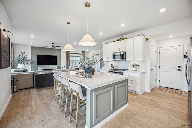 kitchen featuring a breakfast bar, white cabinetry, appliances with stainless steel finishes, light wood-type flooring, and light stone countertops