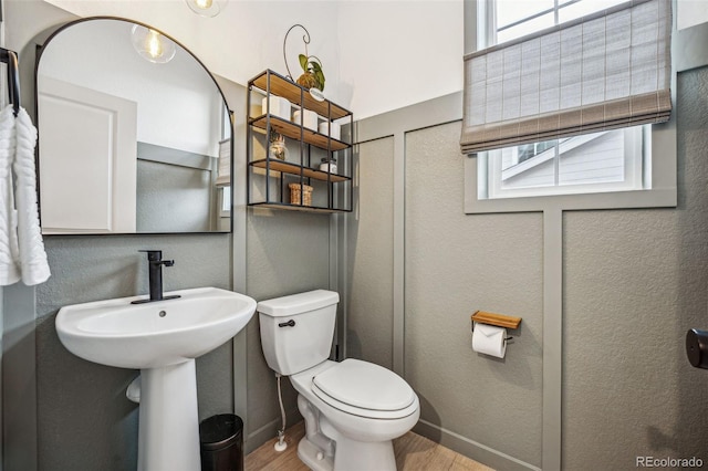 half bathroom with baseboards, a textured wall, toilet, wood finished floors, and a sink