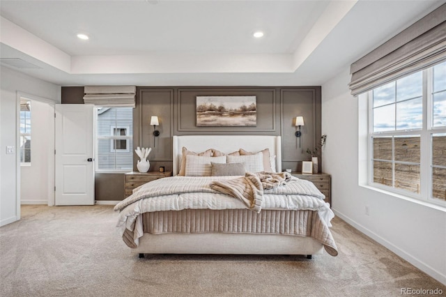 bedroom with baseboards, multiple windows, a raised ceiling, and light colored carpet