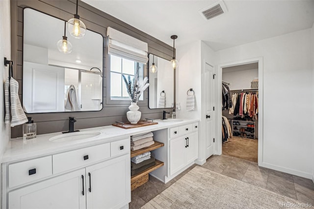 full bathroom featuring double vanity, visible vents, a spacious closet, a sink, and tiled shower