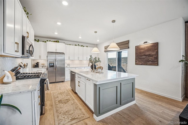 kitchen with appliances with stainless steel finishes, white cabinets, light wood-style floors, and a sink