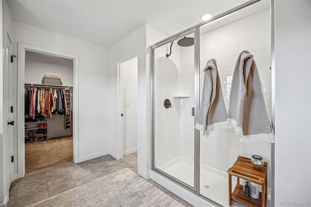 bathroom with a spacious closet, a shower stall, and tile patterned floors