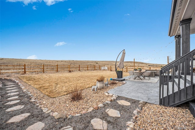 view of yard with a patio area, a fenced backyard, outdoor dining space, and a rural view