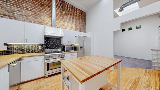 1510 Wazee St Unit 3, Denver, CO 80202 - kitchen with wood counters, appliances with stainless steel finishes, exhaust hood, a high ceiling, and backsplash