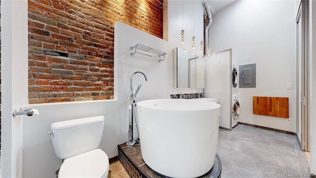 1510 Wazee St Unit 3, Denver, CO 80202 - full bathroom featuring stacked washing machine and dryer, toilet, a towering ceiling, electric panel, and brick wall
