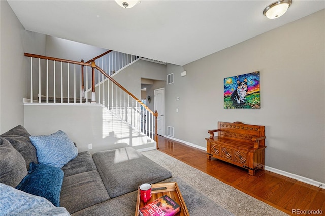 living room featuring wood finished floors, baseboards, visible vents, and stairs