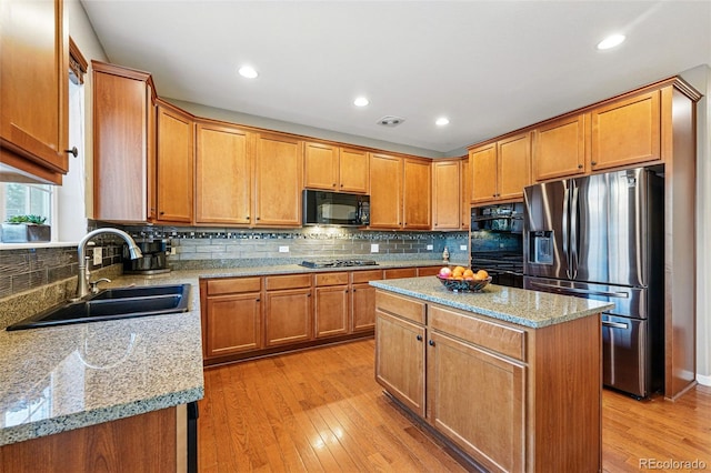kitchen featuring light wood-type flooring, black appliances, light stone counters, a sink, and decorative backsplash