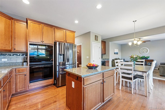 kitchen featuring a center island, light stone countertops, stainless steel refrigerator with ice dispenser, dobule oven black, and light wood-style floors