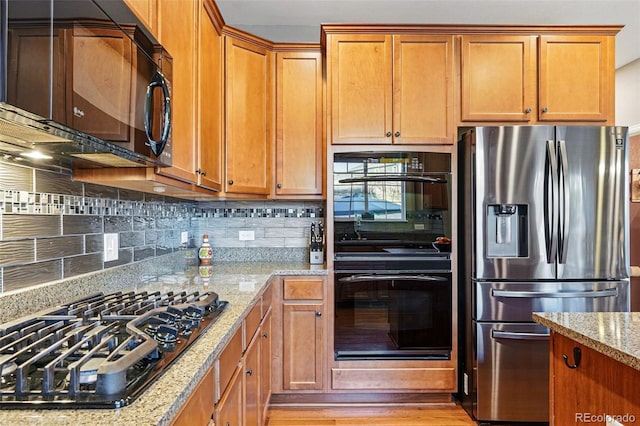 kitchen featuring light stone countertops, brown cabinets, black appliances, and backsplash