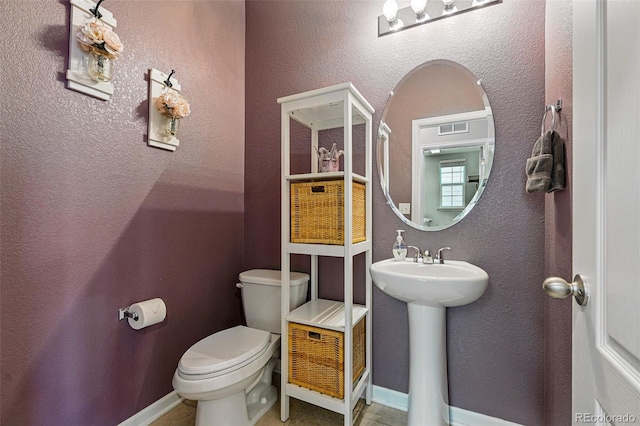 half bathroom featuring a sink, tile patterned floors, toilet, and baseboards