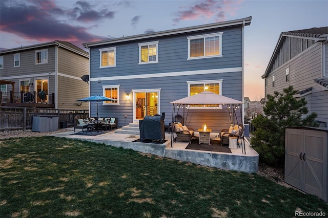 back of property at dusk with an outdoor fire pit, a storage shed, a patio area, and an outbuilding