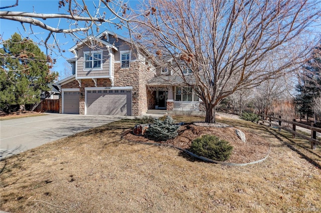 view of front facade with an attached garage, stone siding, concrete driveway, and fence