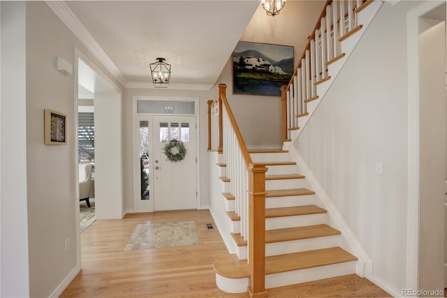 foyer with a chandelier, wood finished floors, visible vents, stairs, and crown molding