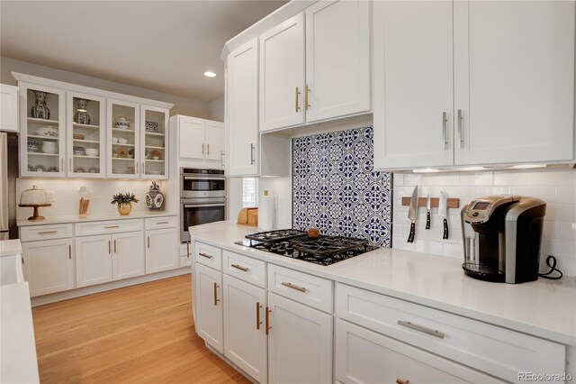 kitchen with appliances with stainless steel finishes, light countertops, white cabinets, and light wood finished floors