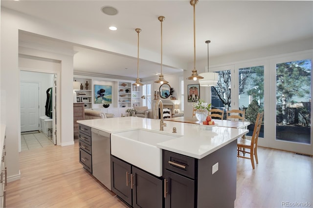 kitchen with open floor plan, hanging light fixtures, light countertops, stainless steel dishwasher, and a sink