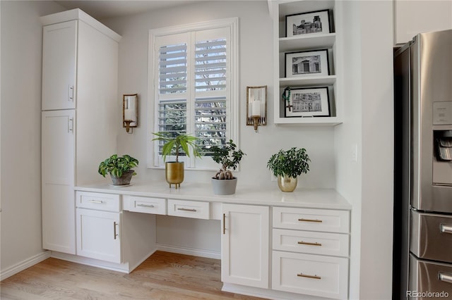 interior space featuring built in desk, stainless steel refrigerator with ice dispenser, light countertops, light wood-style floors, and white cabinets