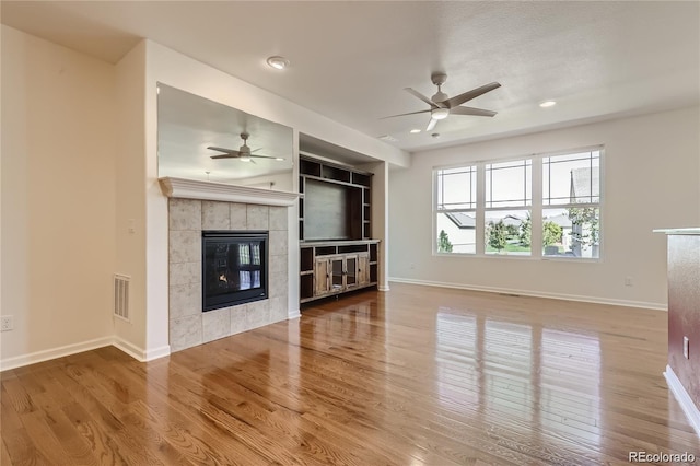 unfurnished living room featuring a tile fireplace, ceiling fan, and hardwood / wood-style flooring