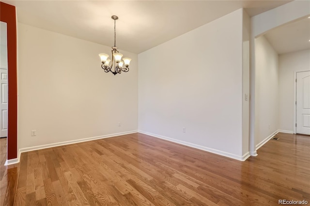 empty room with hardwood / wood-style floors and a notable chandelier