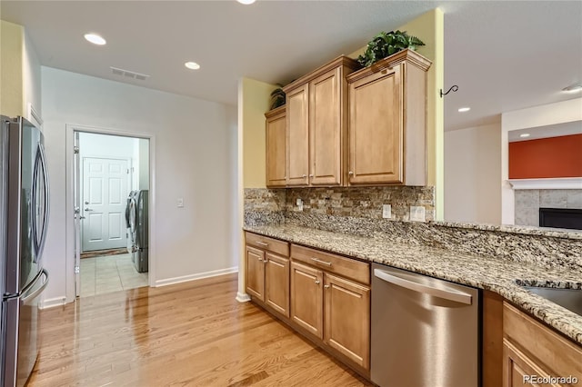 kitchen featuring light stone counters, tasteful backsplash, a fireplace, stainless steel appliances, and light hardwood / wood-style flooring