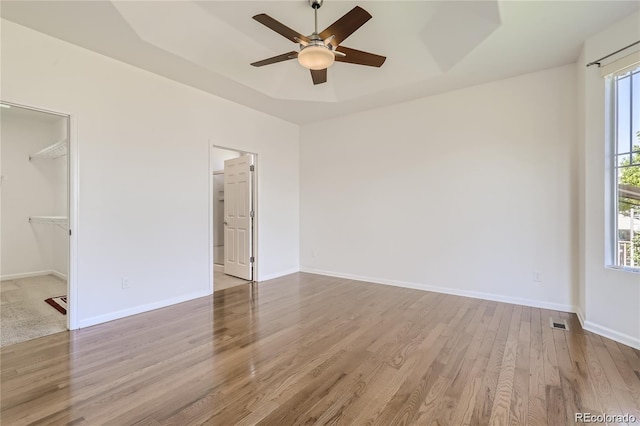 unfurnished bedroom featuring a closet, light hardwood / wood-style floors, a walk in closet, and ceiling fan