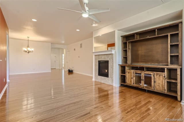 unfurnished living room with wood-type flooring, ceiling fan with notable chandelier, and a tiled fireplace