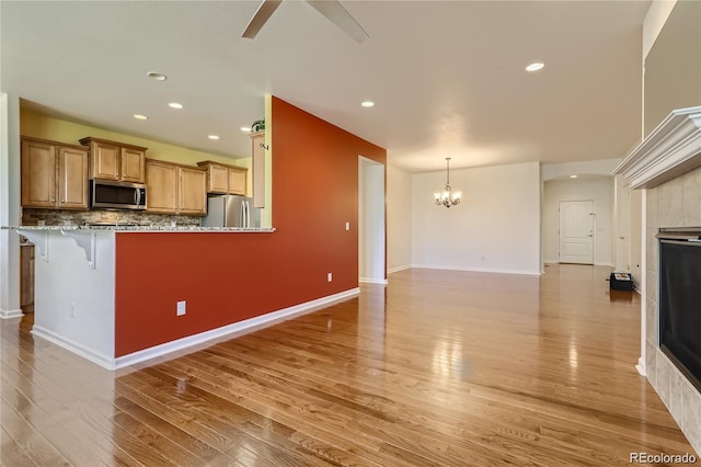 kitchen featuring kitchen peninsula, backsplash, appliances with stainless steel finishes, a breakfast bar, and light hardwood / wood-style floors