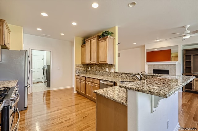 kitchen featuring light wood-type flooring, kitchen peninsula, a kitchen breakfast bar, stainless steel appliances, and light stone countertops