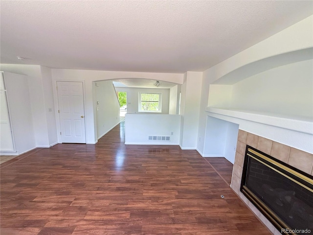 20401 E Chenango Pl, Aurora, CO 80015 - unfurnished living room featuring dark wood-type flooring, arched walkways, a tiled fireplace, and a textured ceiling