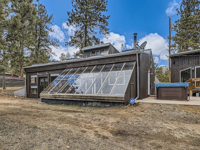 rear view of property with a hot tub and an outbuilding