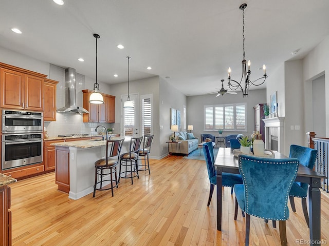 dining area featuring sink, ceiling fan with notable chandelier, and light hardwood / wood-style flooring